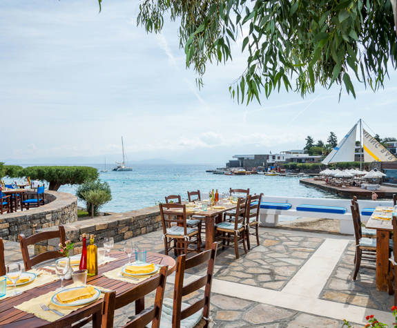 Elounda Bay Palace Ariadne Restaurant tables with the sea and the sail-in bar in the background